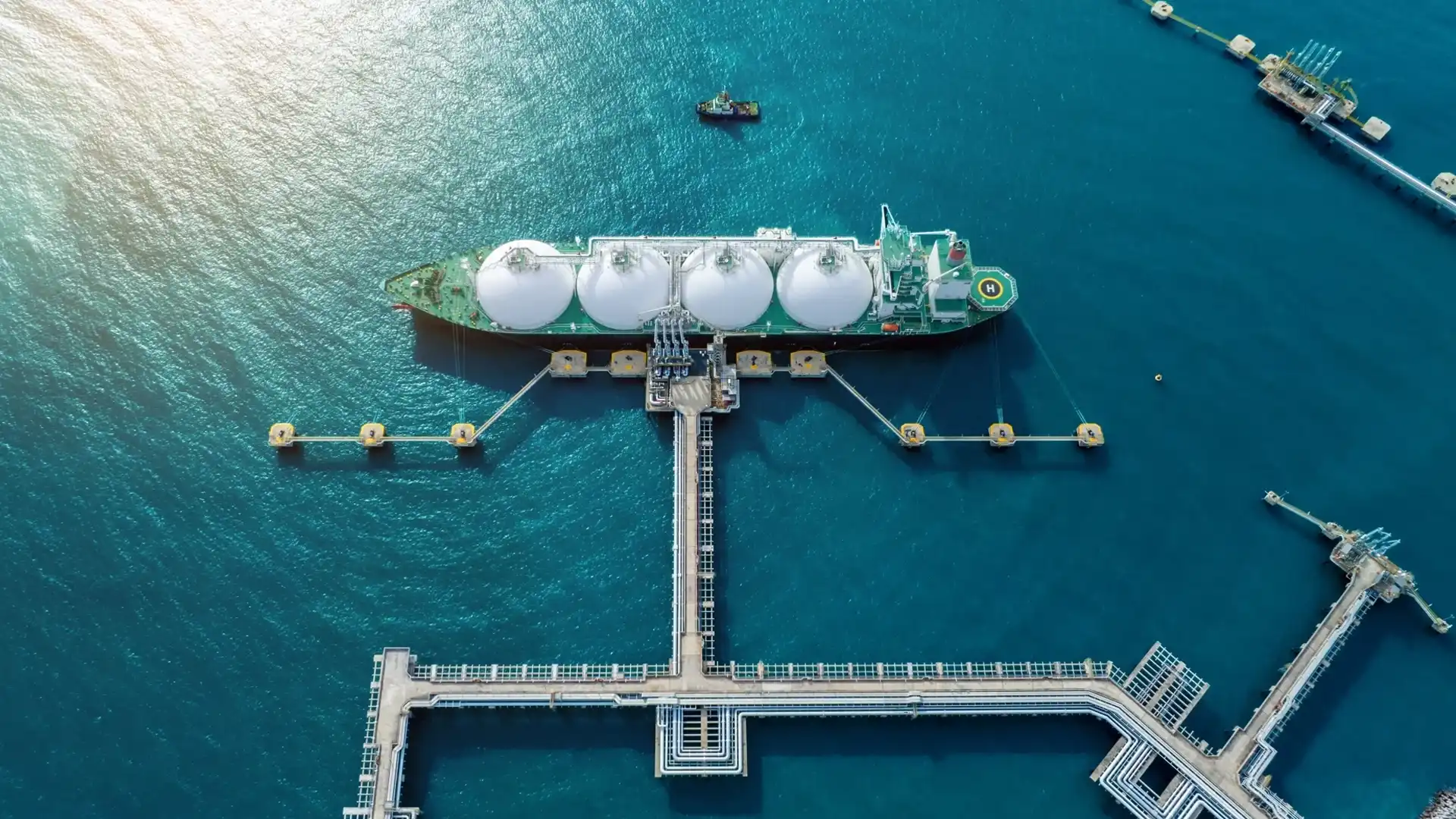 Aerial view of a liquefied natural gas carrier at a port terminal with pipeline connections and offshore infrastructure.